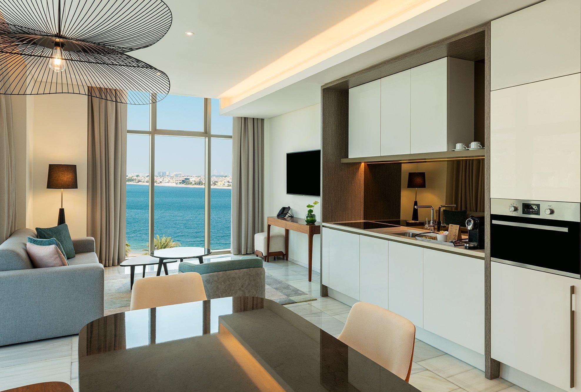 Een moderne hotelkamer met een zithoek, keuken en een groot raam met uitzicht op de stad.