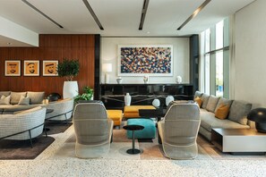 Een moderne woonkamer met een bank, fauteuils, een salontafel en een groot abstract schilderij aan de muur.