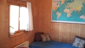 Una habitación de madera con una cama, una silla, una mesa y un mapa mundial en la pared.