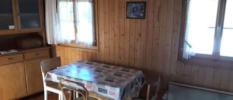 A wooden interior with a dining table, chairs, a cabinet, and windows.