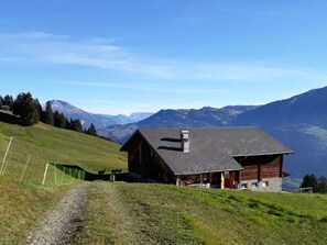 Eine Holzhütte mit geneigtem Dach, gelegen an einem Hang mit freiem Blick auf ferne Berge.