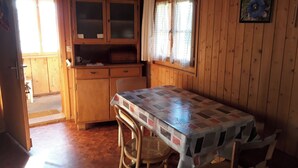 Un interior de madera con una mesa, sillas, un armario y una ventana con cortinas.