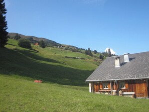 A house with a sloped roof, a porch, and a view of a green hillside. - Maiensäss Rüs, (Präz), by Interhome (Dalin)