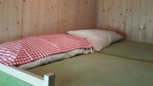 Habitación individual con pared de madera, colchón verde y manta a cuadros rojos y blancos.