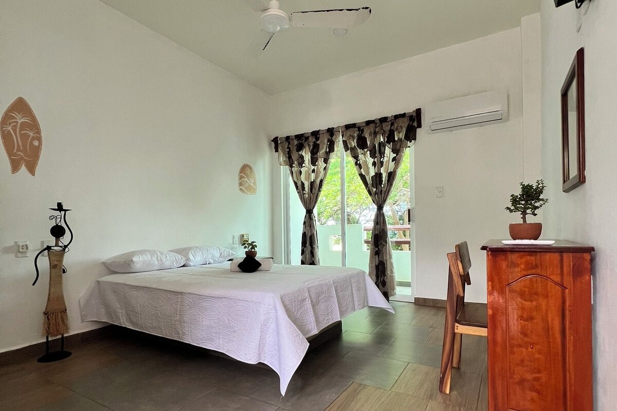 A bedroom with a bed, a ceiling fan, a wooden cabinet, and a window with curtains.