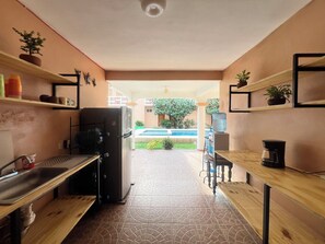 Cozinha compacta com geladeira, pia e mesas de madeira.