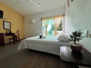 A hotel room with a bed, a desk, a potted plant, and a window with curtains. - Lifestyle Hotel Juquilita - La Punta (Santa María Colotepec)