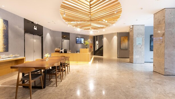 A modern hotel lobby with a reception desk, a seating area with a wooden table and chairs, a large circular wooden ceiling design, and a staircase. - Hanting Hotel Shenzhen Nanshan Avenue Branch (Shenzhen)
