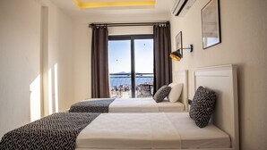 A hotel room with two beds, a large window with curtains, a view of the sea, and a ceiling light. - Lobelya Suites (Kaş)