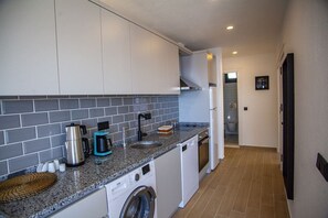 Una cocina compacta con lavadora, cafetera y lavabo.