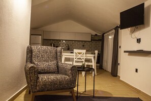 A cozy living area with a patterned armchair, a small table, a white dining table, and a kitchen in the background. - Lobelya Suites (Kaş)