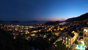 A coastal town at dusk with illuminated buildings and a large swimming pool. - Lobelya Suites (Kaş)