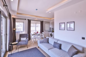 Uma sala moderna com sofá, poltrona, mesa de jantar e uma máquina de lavar roupa ao fundo.