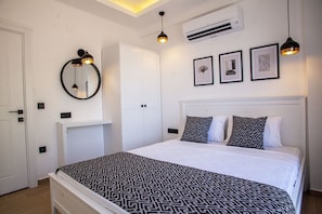 Um quarto com uma cama, um guarda-roupa branco, um espelho redondo e três quadros na parede.