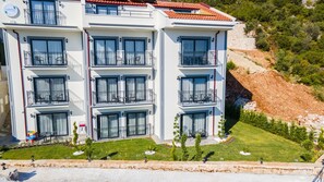 A multi-story hotel with balconies, a well-maintained lawn, and a stone wall in the background. - Lobelya Suites (Kaş)