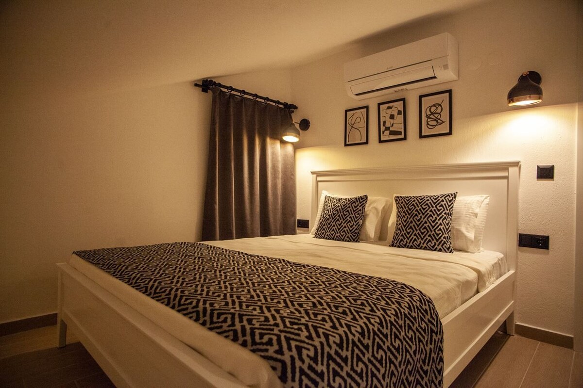 A neatly made bed with patterned bedding, a headboard, and a wall-mounted air conditioner.