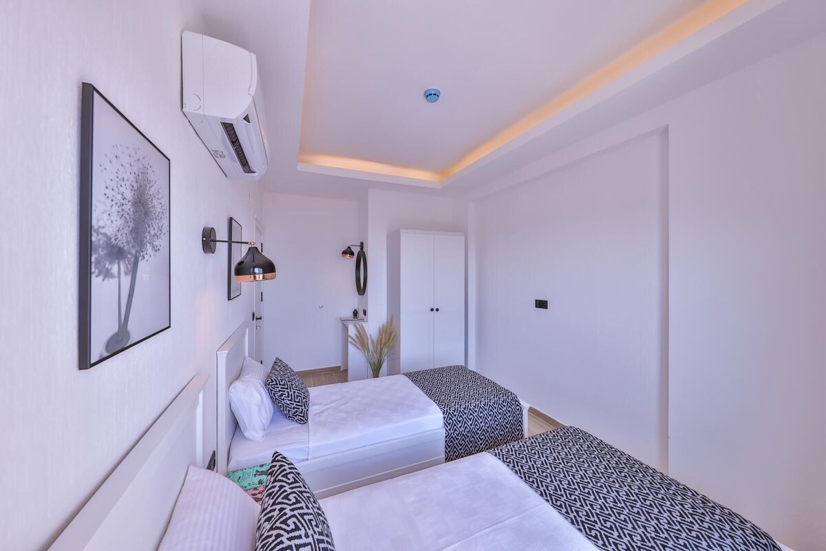 A modern hotel room with two beds, a large window, a wall-mounted air conditioner, and a small desk area.