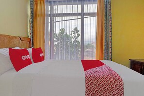 A hotel room with a large bed, two red pillows, a patterned throw, and a view through a large window. - OYO 90488 Harwin Homestay (Batu)