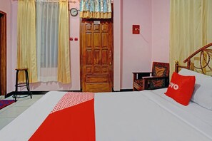 A bedroom with a bed, a wooden door, a small stool, a clock, and a framed picture on the wall. - OYO 90488 Harwin Homestay (Batu)