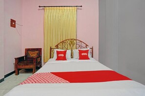 Una cama con una colcha roja y blanca, dos almohadas rojas con el texto 'OYO', una silla de madera y una cortina amarilla.