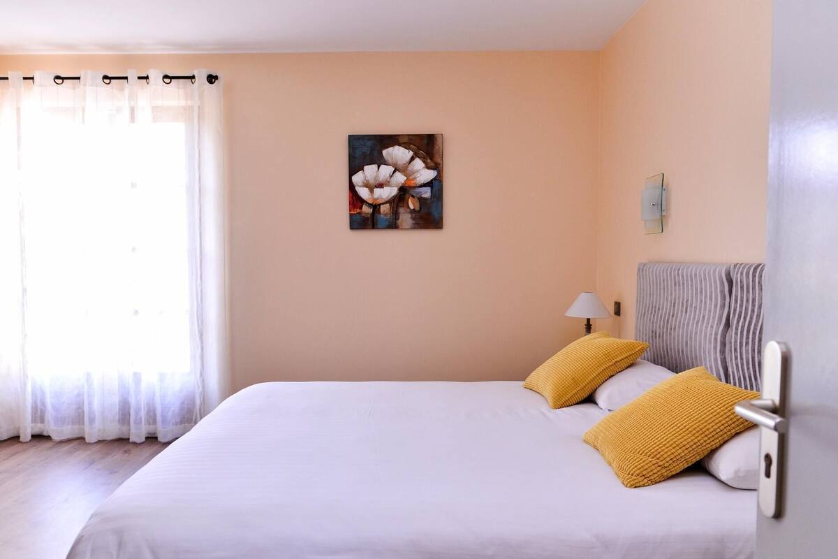 Una habitación de hotel con una cama, un cuadro en la pared y una ventana con cortinas.