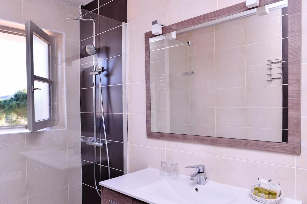 Un baño con ducha, lavamanos, espejo y ventana.