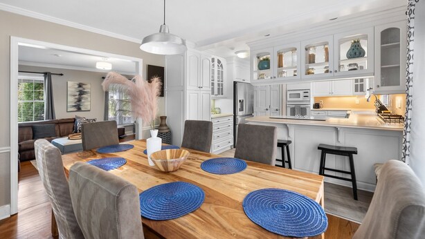 Een moderne keuken met witte kastjes, een houten eettafel met blauwe placemats en een hangende吊灯.