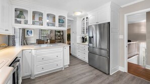 Een keuken met witte kasten, een roestvrijstalen koelkast en een houten vloer.