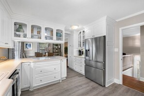 Une cuisine avec des meubles blancs, un réfrigérateur en acier inoxydable et un plancher en bois.
