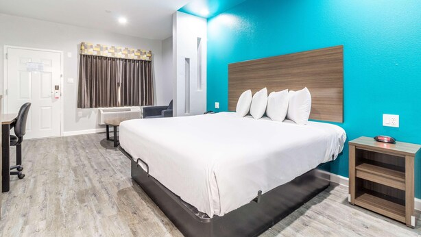 A hotel room with a bed, a desk, a chair, a nightstand, and a wall-mounted air conditioner. - Scottish Inns & Suites Kingwood (Kingwood)