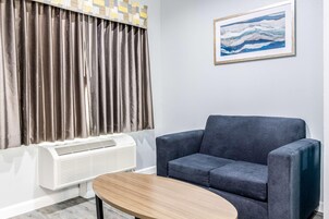 A room with a grey sofa, a wooden coffee table, a white air conditioner, and a painting on the wall.