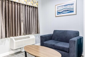 Ein Zimmer mit grauem Sofa, einem hölzernen Couchtisch, einer weißen Klimaanlage und einem Gemälde an der Wand.