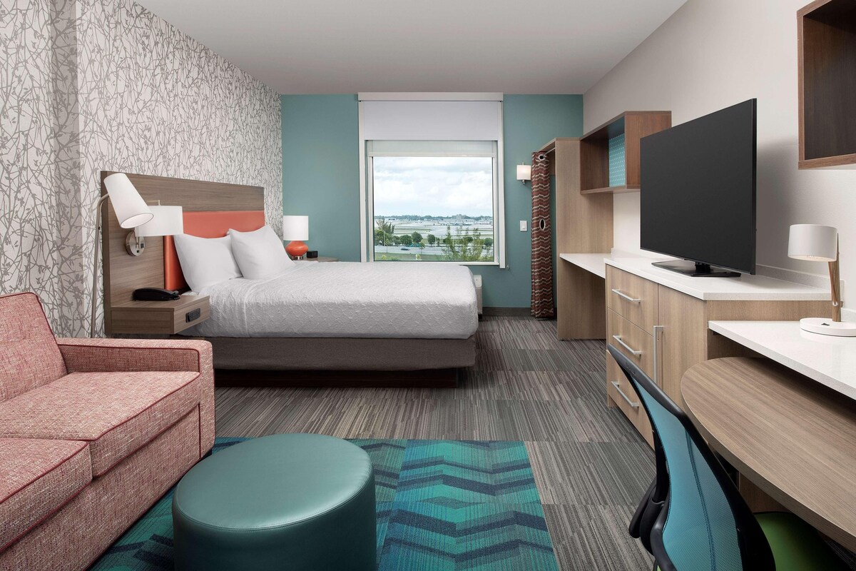 A hotel room with a bed, a sofa, a TV, a desk, and a window with a view.