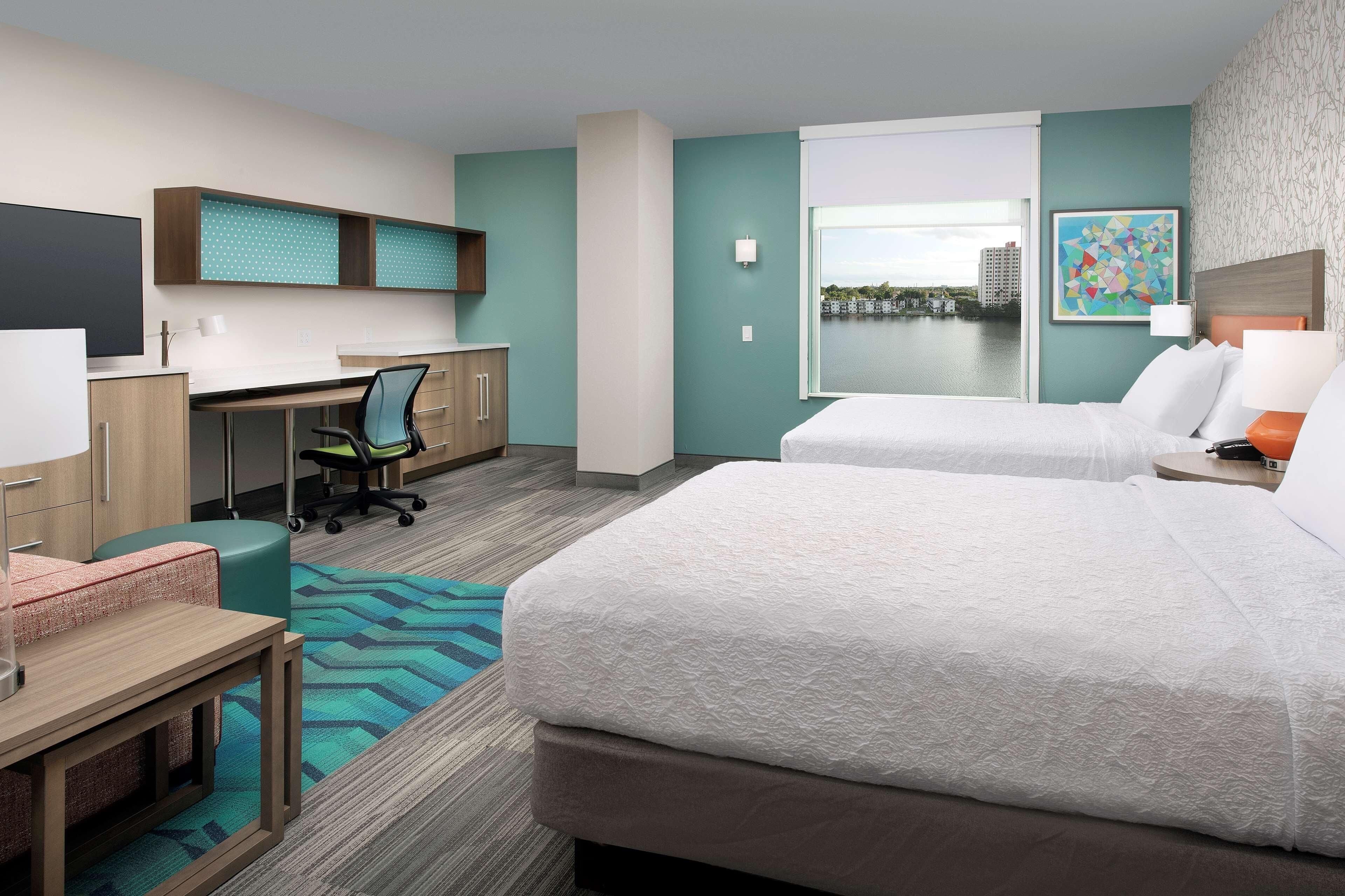 A hotel room with a bed, desk, chair, and a view of the city.