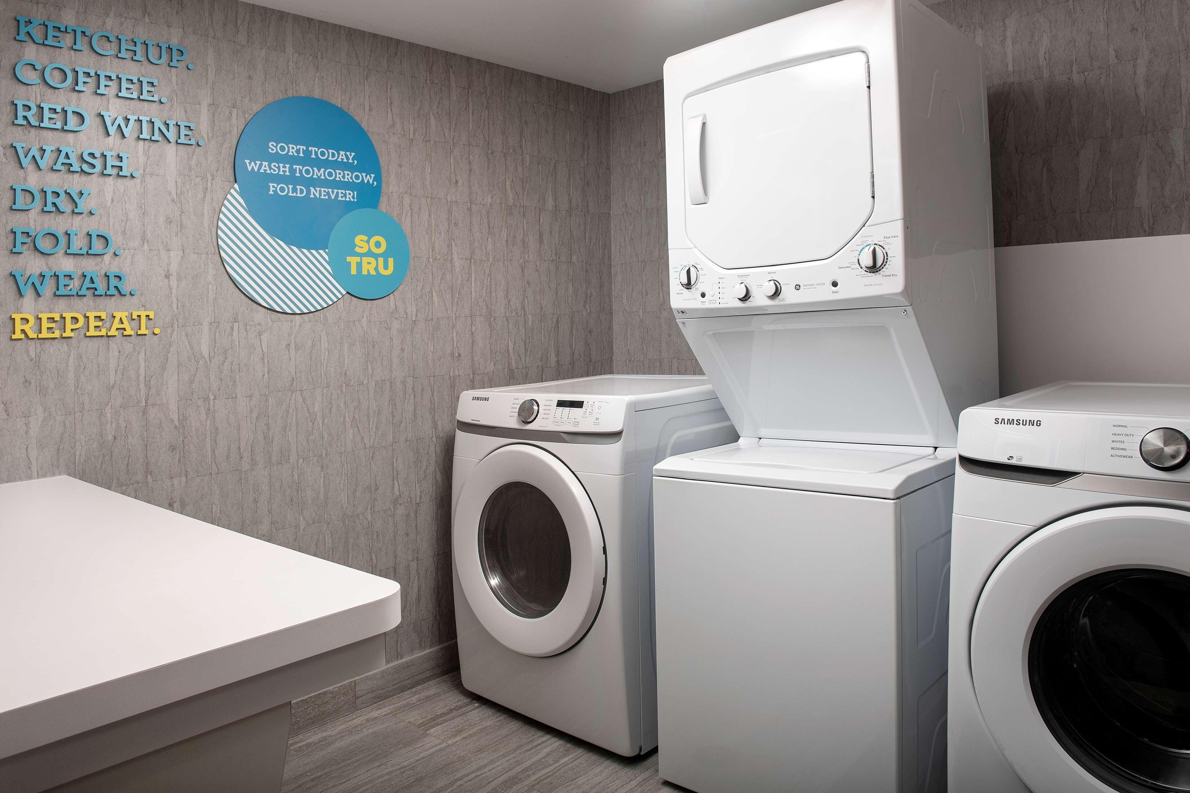 Una sala de lavandería con dos lavadoras, una Samsung y otra genérica, y una pared con un cartel de instrucciones para la ropa.