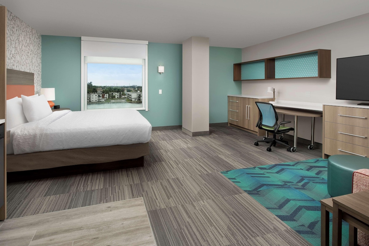 A hotel room with a bed, desk, chair, and a view of the city.