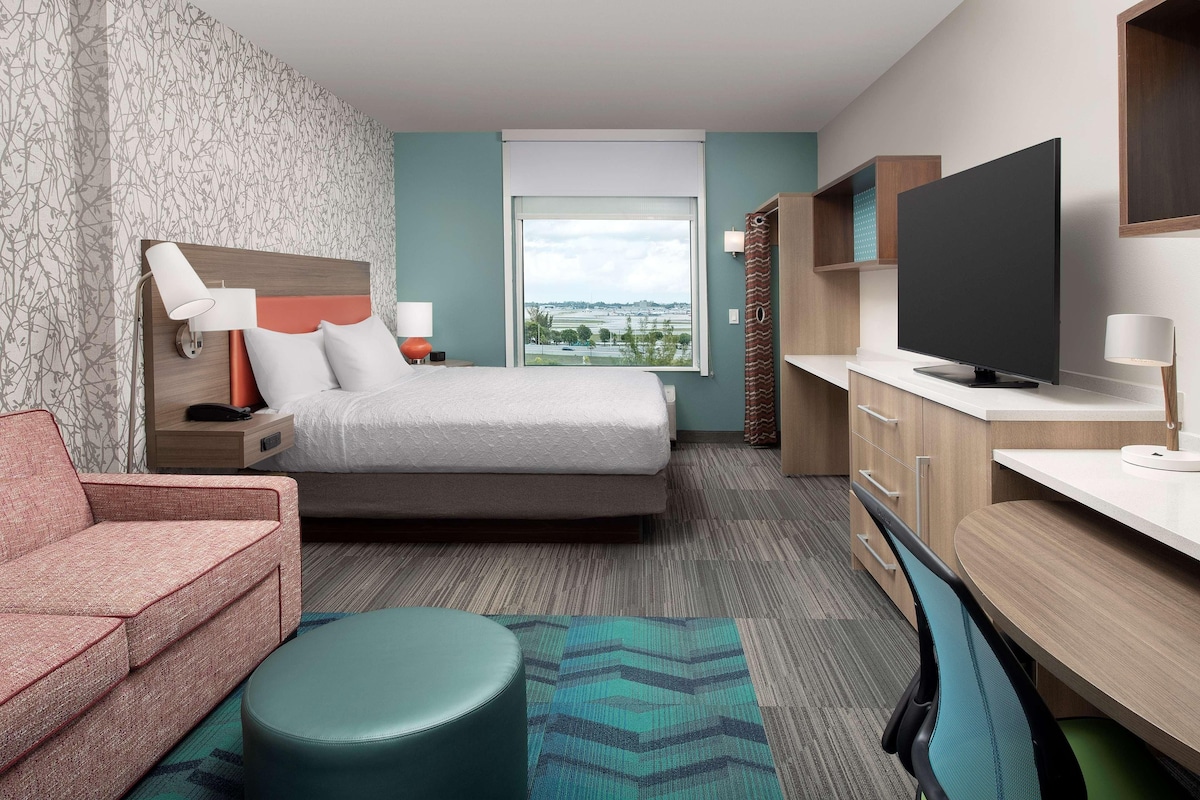 A hotel room with a bed, a sofa, a TV, a desk, and a window with a view.