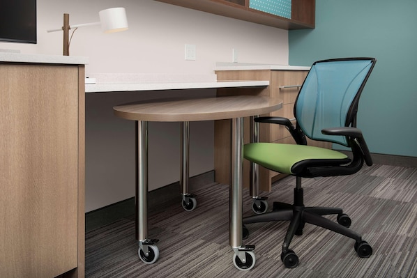 Una silla de oficina moderna sobre ruedas, un escritorio con superficie blanca y una pequeña mesa.