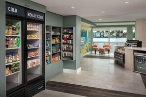 Un hall d’hôtel doté d’un réfrigérateur pour boissons fraîches, d’étagères remplies de collations, d’une fresque murale, d’un espace salon et offrant une vue sur l’eau.