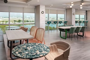A modern hotel lobby with large windows, multiple seating areas, and a view of the airport. - Home2suites by Hilton Miami Airport S. Blue Lagoon (Miami)