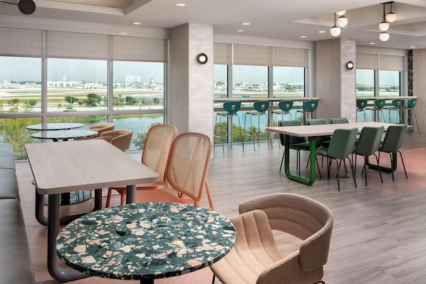 A modern hotel lobby with large windows, multiple seating areas, and a view of the airport. - Home2suites by Hilton Miami Airport S. Blue Lagoon (Miami)