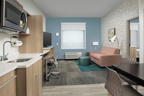 Une chambre d’hôtel compacte comprenant un coin cuisine, un canapé, une table à manger et un téléviseur.
