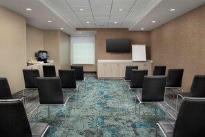 Una sala de conferencias con alfombra estampada, sillas negras, una estación de café, una pizarra y un televisor en la pared.