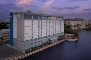 A multi-story hotel with a parking garage, located near a body of water. - Home2suites by Hilton Miami Airport S. Blue Lagoon (Miami)