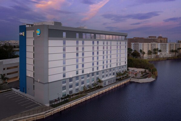 A multi-story hotel with a parking garage, located near a body of water. - Home2suites by Hilton Miami Airport S. Blue Lagoon (Miami)