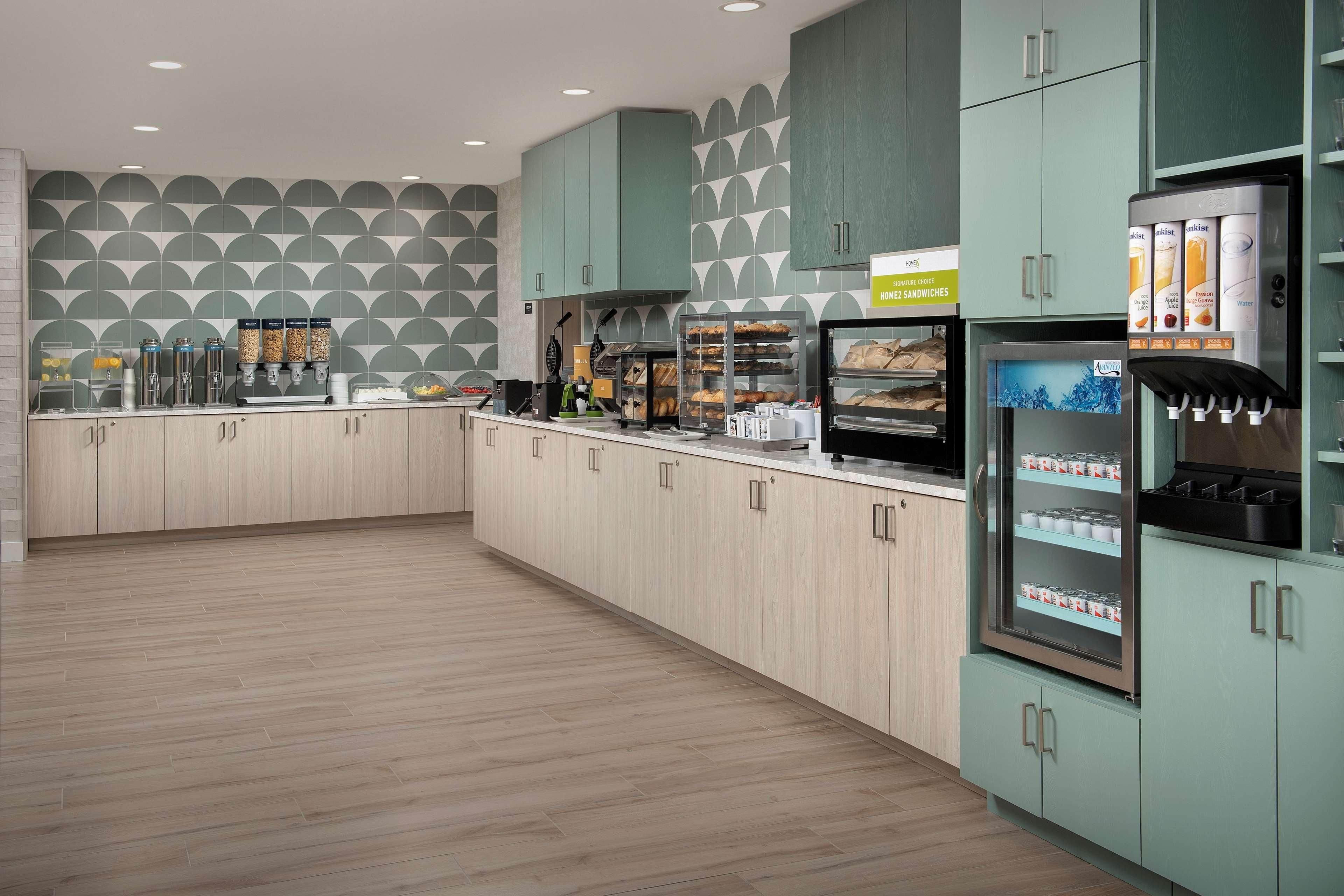 A modern kitchen with light wood cabinets, a coffee station, and a refrigerator with a beverage dispenser.