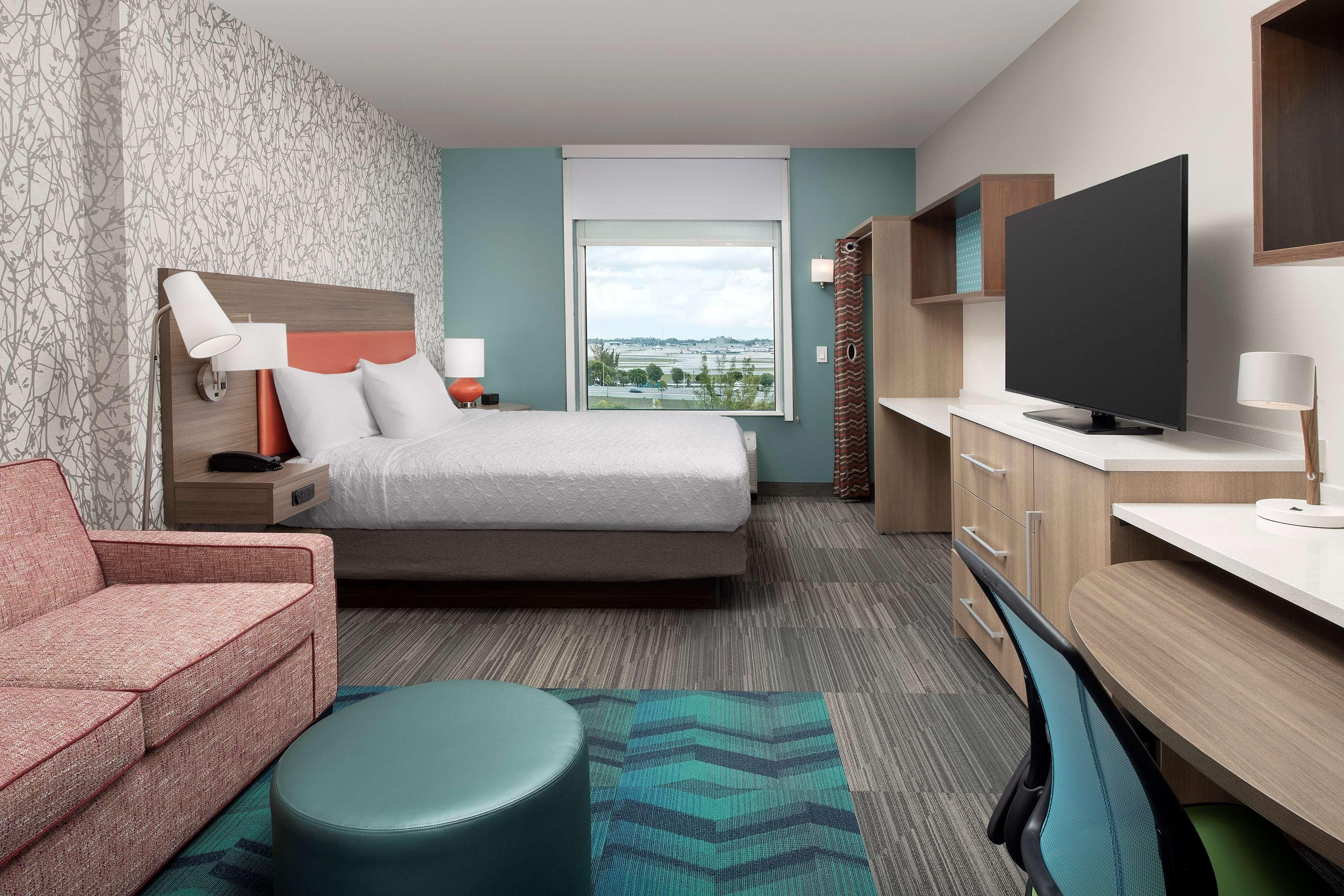 A hotel room with a bed, a sofa, a TV, a desk, and a window with a view.