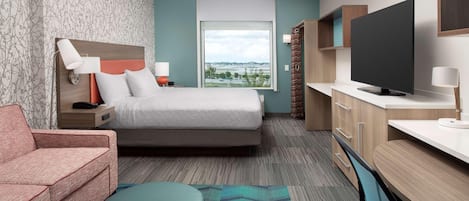 A hotel room with a bed, a sofa, a TV, a desk, and a window with a view.