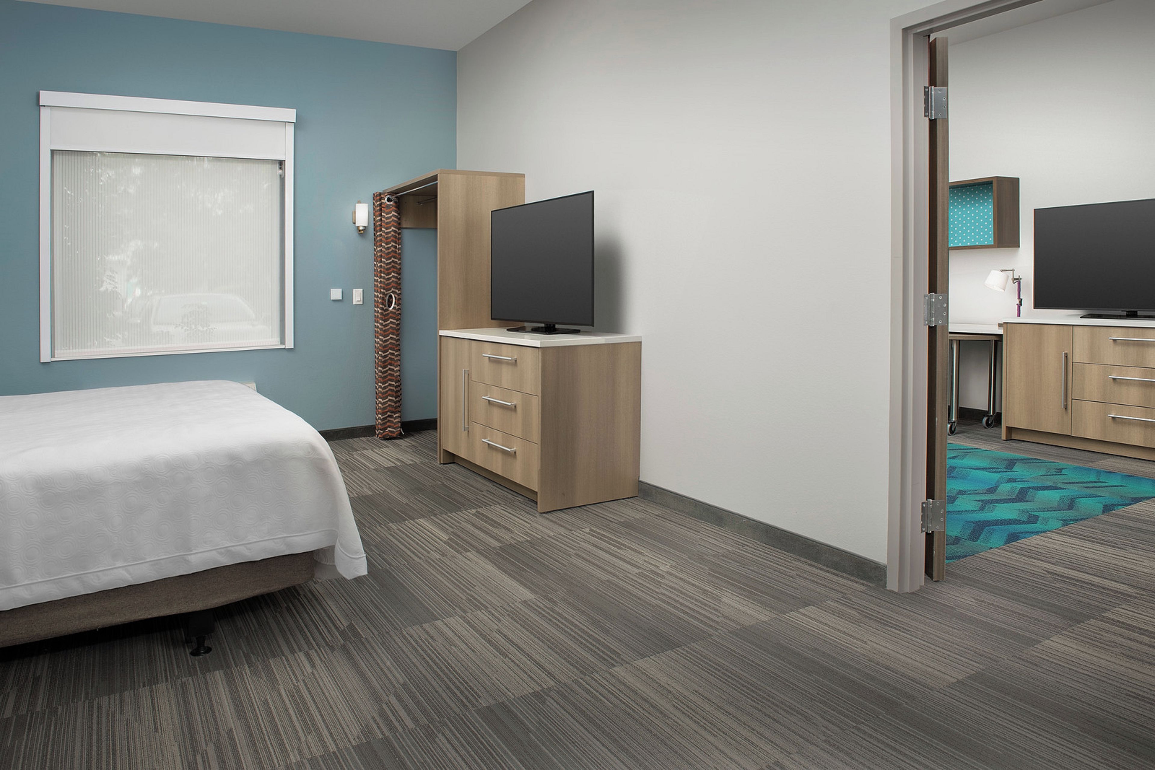 A hotel room with a bed, a TV on a wooden cabinet, a bathroom with a mirror and a toilet, and a patterned rug.