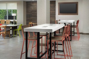 A conference room with multiple tables and chairs, a large screen, and a window with a view. - Home2suites by Hilton Miami Airport S. Blue Lagoon (Miami)